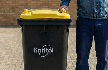 Eine Person steht neben einer Gelben Tonne mit der Aufschrift "Knittel"