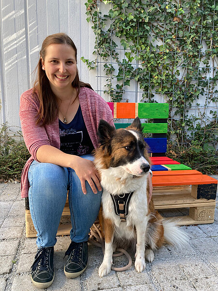 Bibliothekarin Julia Schmid sitzt neben ihrer Büchereihündin Anuk und lächelt in die Kamera
