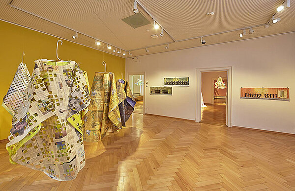 In einem Ausstellungsraum im Museum hängen aus Zeitungspapier und anderen Materialien gestaltete Gewänder.