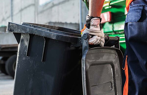 Eine Person mit Arbeitshandschuhen schiebt eine Mülltonne