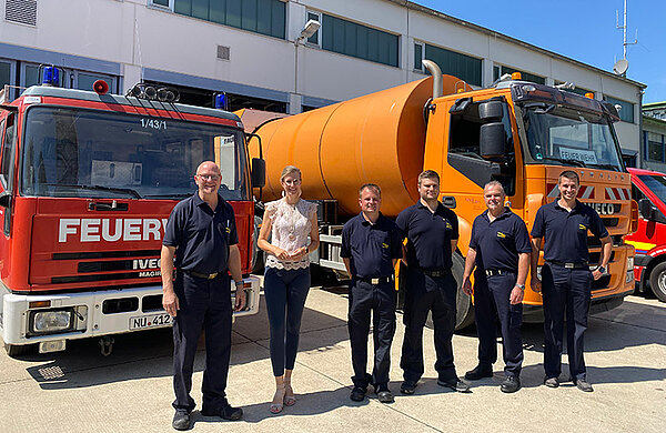 Der stellvertretende Leiter der Feuerwehr und Neu-Ulms Oberbürgermeisterin gemeinsam mit vier Feuerwehr-Kameraden vor einem Feuerwehrfahrzeug und einem Müllfahrzeug