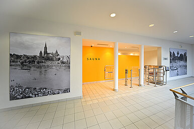 Eingang zum Saunabereich mit dem Schriftzug "Sauna" auf einer gelben Wand, im Vordergrund eine Schwarz-Weiß-Fotografie von der Donau mit Blick nach Ulm