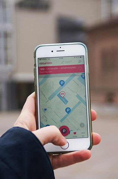 Eine Hand hält ein Smartphone. Auf dem Bildschirm zeigt die EasyPark-App Parkmöglichkeiten in der Neu-Ulmer Innenstadt an.