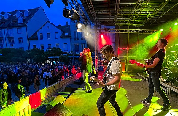 Eine Liveband spielt beim Stadtfest auf einer Bühne vor dem Publikum auf dem Petrusplatz.