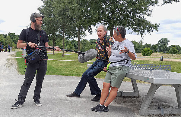 Ein Mann mit Kopfhörer hält einem Mann und einer Frau ein Mikrophon hin.