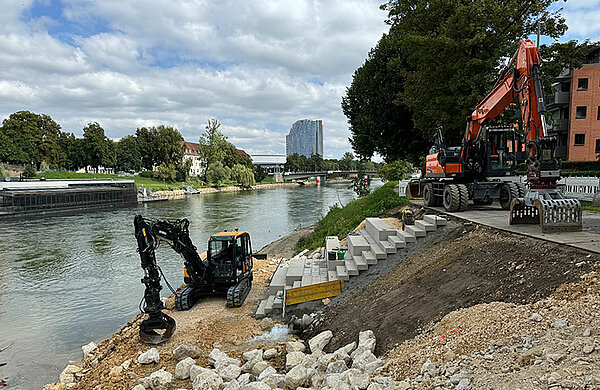 Bagger an der Baustelle am Neu-Ulmer Donauufer, wo bereits ein Teil der neuen Sitzstufen zu sehen ist.