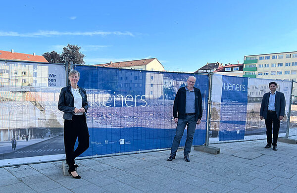 Oberbürgermeisterin Katrin Albsteiger, Berthold Stier und Thomas Niederberger vor den neuen Bauzaunbannern. Hinter ihnen die Baustelle, wo das Heiners gebaut werden soll.