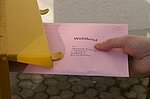 Abbildung eines Briefwahl-Umschlages, der gerade in einen Briefkasten geworfen wird.