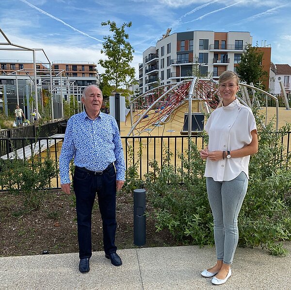 Neu-Ulms Oberbürgermeisterin Katrin Albsteiger und Bois-Colombes Bürgermeister Yves Révillion stehend vor der Kamera, im Hintergrund ein Spielplatz