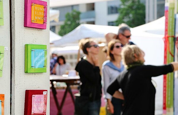 Stand mit bunten Bildern, im Hintergrund Marktbesucher