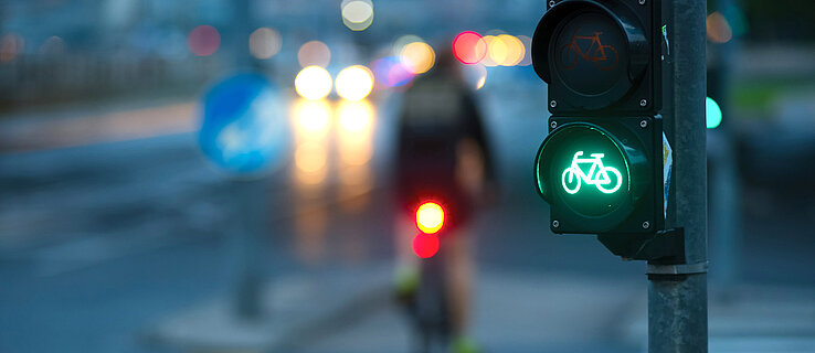 Ein Radfahrer fährt mit seinem beleuchteten Fahrrad an einer Fahrradampel mit grünem Fahrradsymbol vorbei