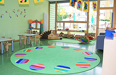 Kita-Gruppenraum mit Tischen und Spielecke