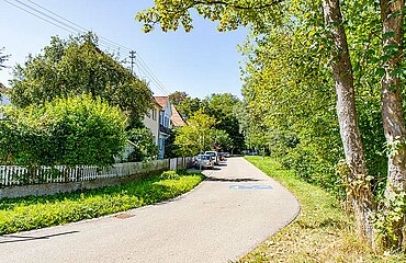 Wohnhäuser, Autos, Bäume und Sträucher an einer Straße mit dem blauen Aufdruck "Spielstraße" auf der Fahrbahn