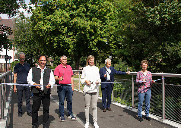Oberbürgermeisterin Katrin Albsteiger steht zusammen mit Vertretern des Stadtrates, der Baufirma und der Verwaltung auf der neuen Brücke und schneidet das symbolisch gespannte Band durch.