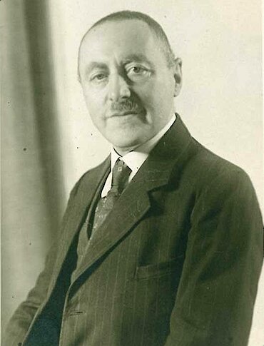 Alfred Neuburger mit mittlerem Alter in Anzug und Krawatte
