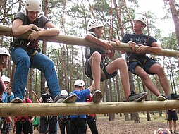 Drei Jugendliche klettern gemeinsam eine Riesenleiter hinauf.