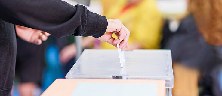 Eine Person wirft einen Stimmzettel in eine Wahlurne.