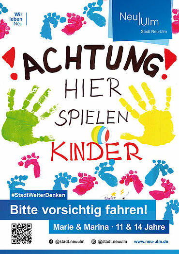 Schild mit dem Text "Achtung! Hier spielen Kinder. Bitte vorsichtig fahren!" und bunten Hand- und Fußabdrücken