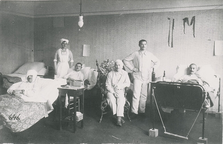 Schwarz-weiß-Foto von einem Krankenzimmer im Lazarett mit fünf Patienten und Pauline Elisabetha Rosenstiel als Krankenschwester