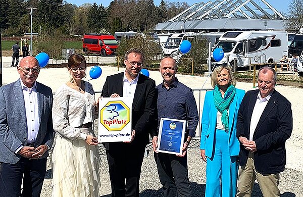 Gruppenfoto auf dem Wohnmobil-Stellplatz: Der Ulmer Oberbürgermeister und die Neu-Ulmer Oberbürgermeisterin halten eine Tafel mit der Aufschrift "Top Platz" in ihren Händen, neben ihnen weitere Beteiligte.