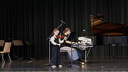 Kind mit Geige neben einer Frau am Klavier