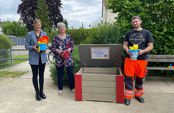 Sandzeugspielkiste mit geöffnetem Deckel, drumherum stehend Neu-Ulms Oberbürgermeisterin Katrin Albsteiger, Iris Stieglitz, Abteilungsleiterin Grünflächen und Friedhof, und der Schreiner Markus Winkler vom städtischen Baubetriebshof