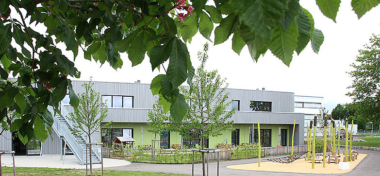 Außenansicht des Kinderhauses Abenteuerland mit Bäumen und Spielplatz