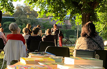 Lesung im Freien vor Publikum, im Vordergrund ein Tisch mit Büchern