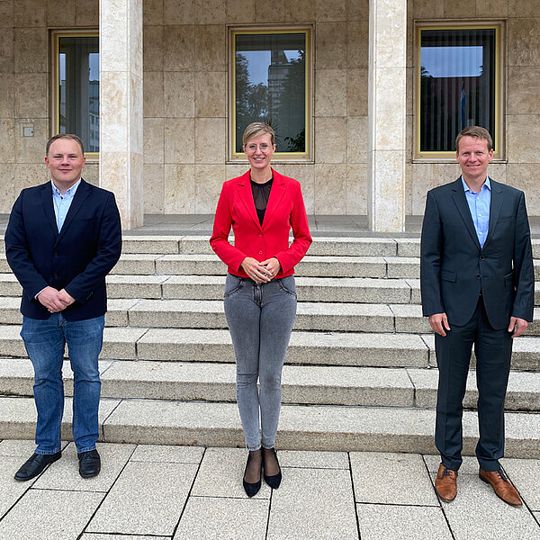 Oberbürgermeisterin Katrin Albsteiger und die beiden neuen Mitarbeiter stehen vor dem Rathaus und lächeln in die Kamera.