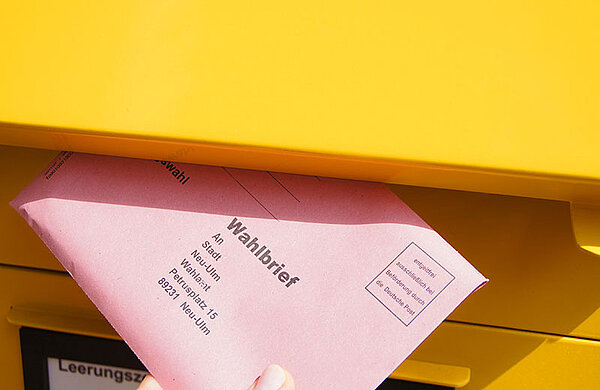 Ein Umschlag mit Briefwahlunterlagen wird in einen Briefkasten geworfen.