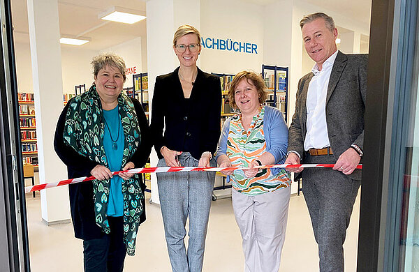 Oberbürgermeisterin Katrin Albsteieger, Dezernent Ralph Seiffert und die beiden Mitarbeiterinnen der Bücherei schneiden ein rotes Band an der Eingangstür zur Bücherei durch.