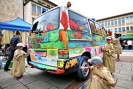 Kinder in Malkitteln malen ein Polizeiauto mit den Händen mit bunten Farben an.