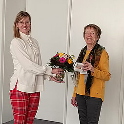 Marieluise Polte hält die Ehrenmedaille für Pflege in die Kamera, Oberbürgermeisterin Katrin Albsteiger überreicht ihr einen Blumenstrauß.
