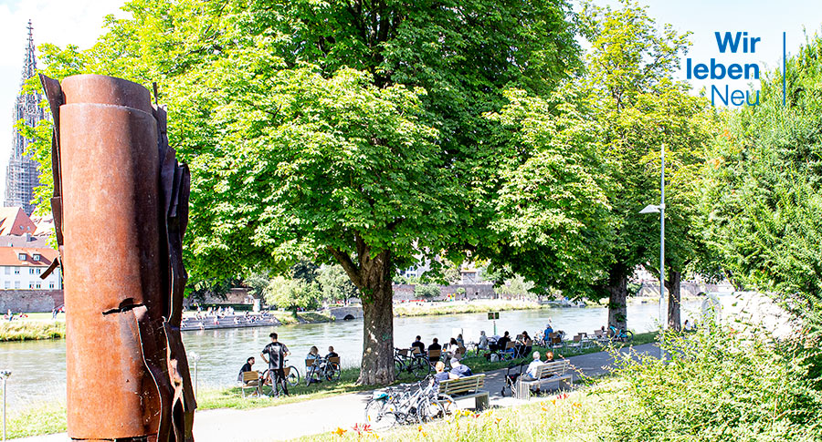 Menschen sitzen zusammen am Neu-Ulmer Donauufer auf Stühlen und Parkbänken