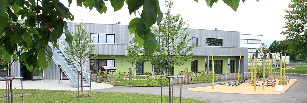 Außenansicht des Kinderhauses Abenteuerland, im Vordergrund Bäume und ein Spielplatz