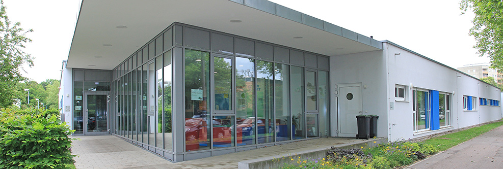 Außenansicht des Kinderhauses Abenteuerland, im Vordergrund Bäume und ein Spielplatz