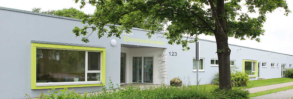 Außenansicht des Kinderhauses Abenteuerland, im Vordergrund Bäume und ein Spielplatz