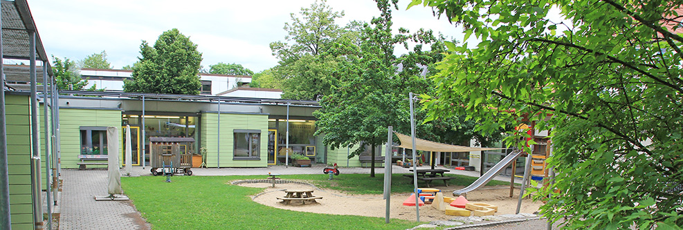 Außengelände der Kindertagesstätte mit Spielplatz und Bäumen