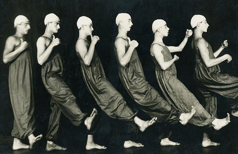 Schwarz-Weiß-Foto mehrerer seitlich schreitender Tänzer