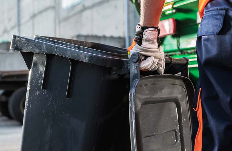 Eine Person mit Arbeitshandschuhen schiebt eine Mülltonne