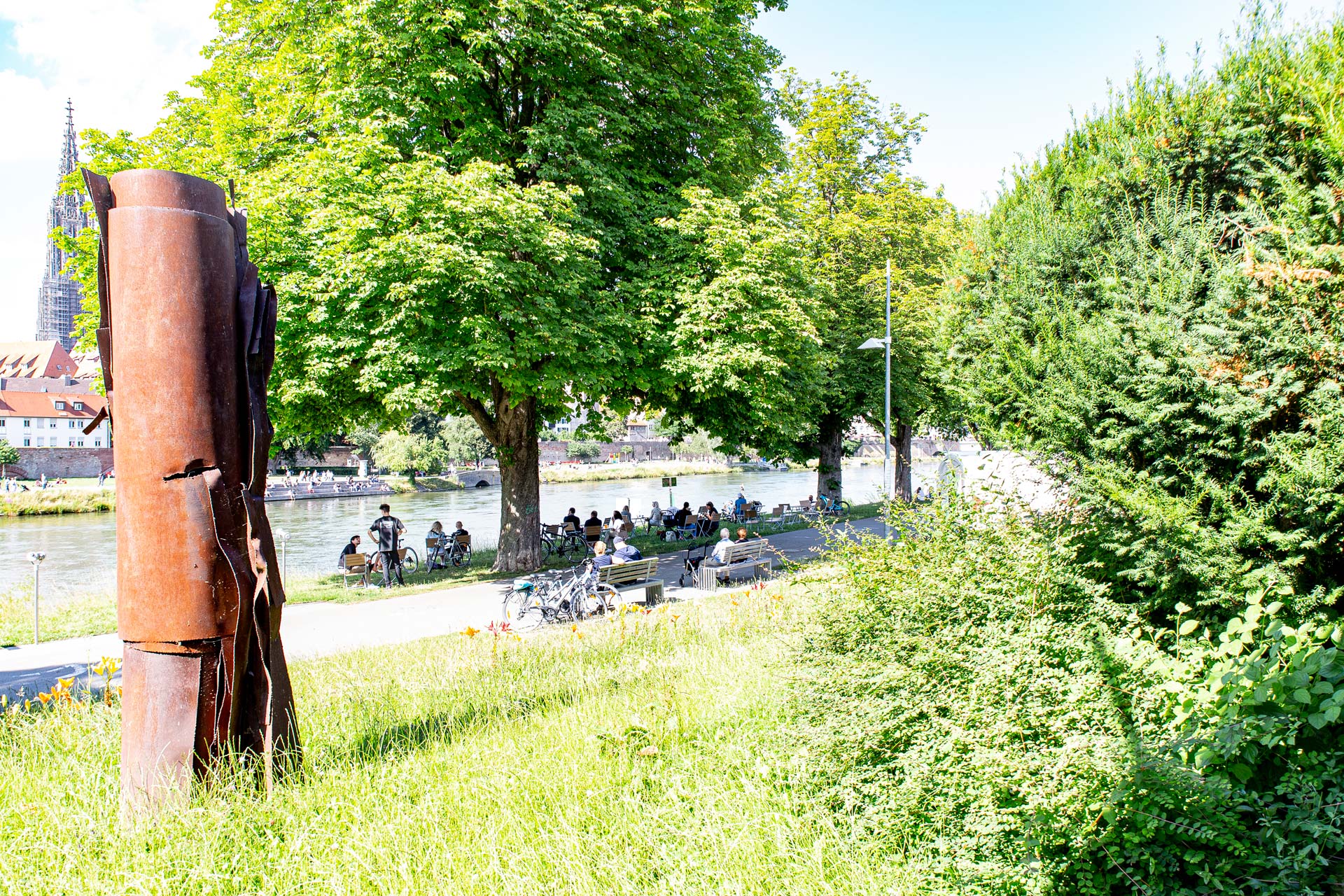 Menschen sitzen am Neu-Ulmer Donauufer