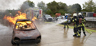 Feuerwehrleute löschen ein brennendes Auto