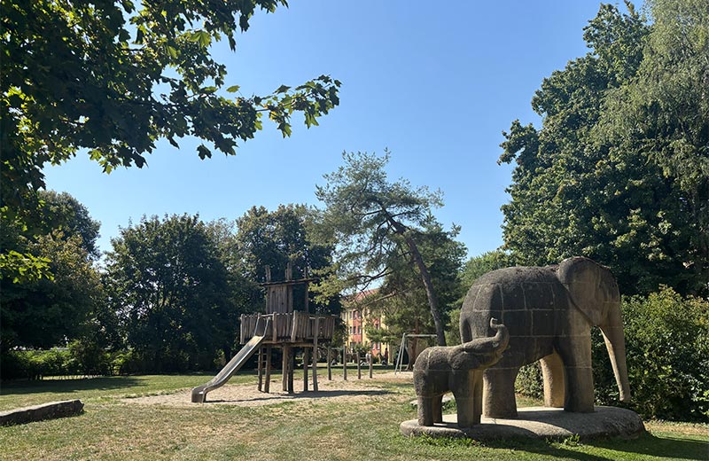 Grünfläche mit großen Skulpturen in Form von Elefanten sowie einem Spielplatz