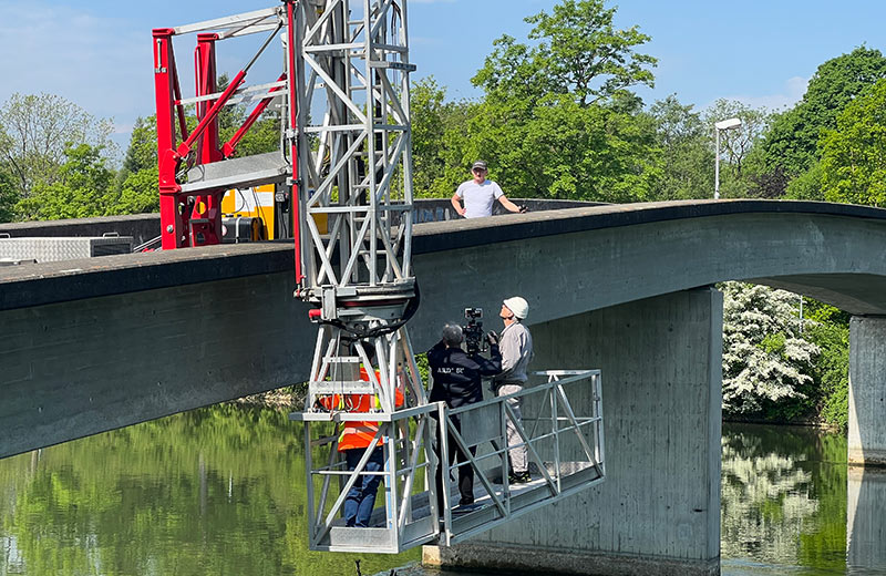 Arbeiten stehen auf einer Hebebühne, die an einer Brücke befestigt ist.