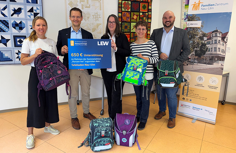 5 Personen mit bunten Schulranzen und einem großen Scheck