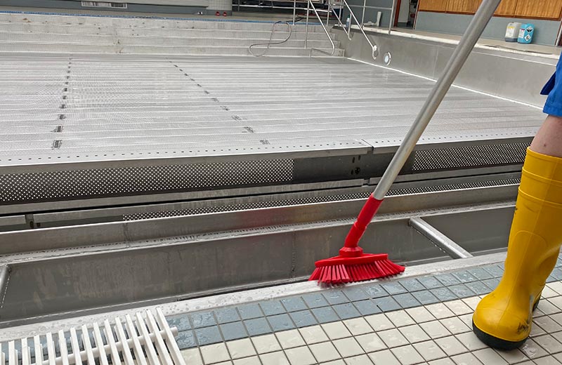 Der Beckenrand eines Schwimmbeckens wird mit einer Bürste gereinigt.