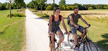 Eine Frau und ein Mann fahrren in kurzer sommerlicher Bekleidung auf einem gekiesten Fahrradweg durch eine grüne Landschaft