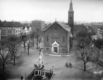 Schwarz-weiß-Fotografie von Platz mit Kirche und großem Wohnhaus am linken Rand