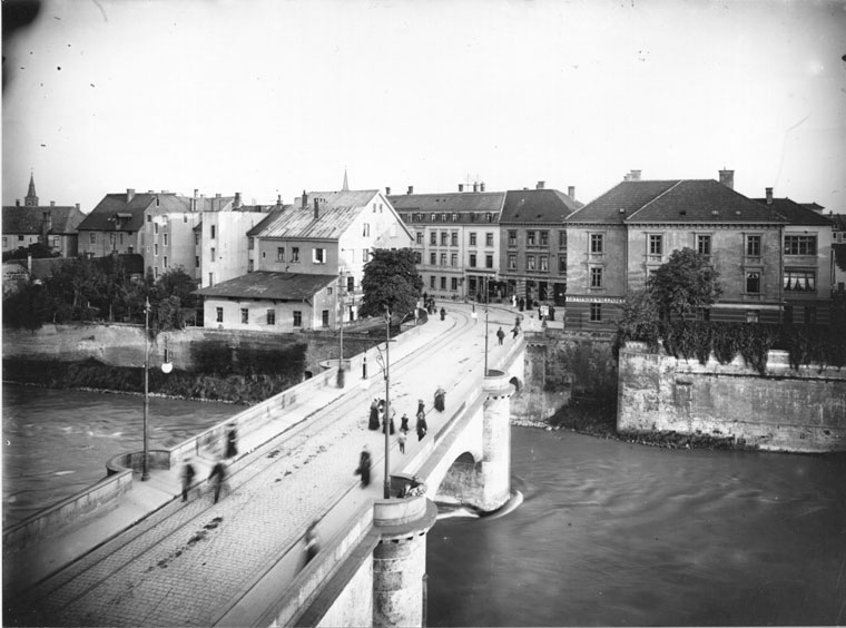 Schwarz-Weiß-Fotografie, Aufnahme von oben, Blick auf eine Brücke (mit Passanten) über einen Fluss (Donau), die Straße führt nach Neu-Ulm