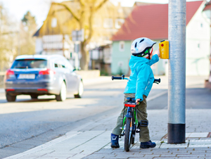 Ein kleines Kind auf einem Fahrrad drückt auf einen Ampeltaster